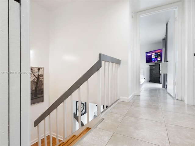 hallway with light tile patterned floors, baseboards, and an upstairs landing