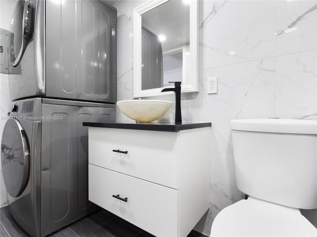 bathroom featuring toilet, stacked washer / dryer, vanity, and tile walls