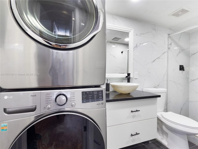 laundry area with laundry area, a sink, visible vents, tile walls, and stacked washing maching and dryer