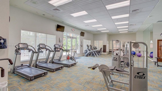 exercise room featuring a paneled ceiling, carpet flooring, visible vents, and a high ceiling