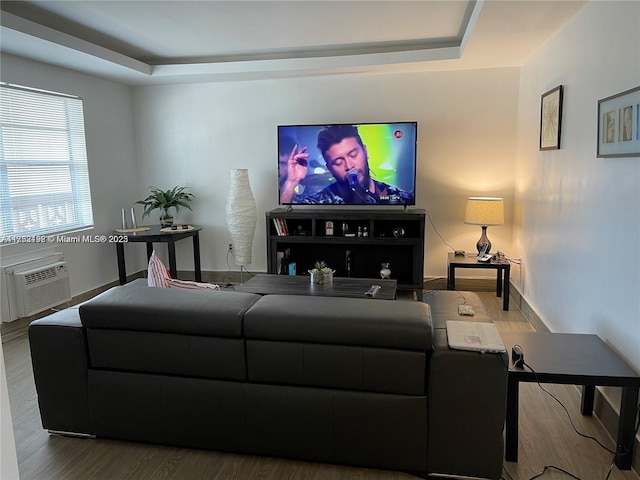 living room featuring a raised ceiling, a wall unit AC, baseboards, and wood finished floors