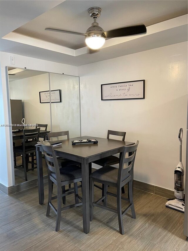 dining area featuring dark wood-style floors, a raised ceiling, baseboards, and a ceiling fan