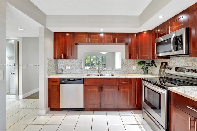 kitchen featuring a sink, light tile patterned floors, decorative backsplash, stainless steel appliances, and reddish brown cabinets