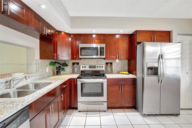 kitchen with light stone counters, a sink, appliances with stainless steel finishes, reddish brown cabinets, and backsplash