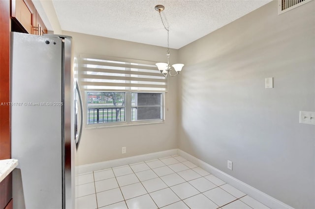 unfurnished dining area with a textured ceiling, light tile patterned floors, visible vents, baseboards, and an inviting chandelier