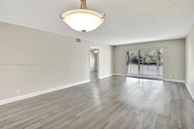 unfurnished room with visible vents, a textured ceiling, baseboards, and wood finished floors