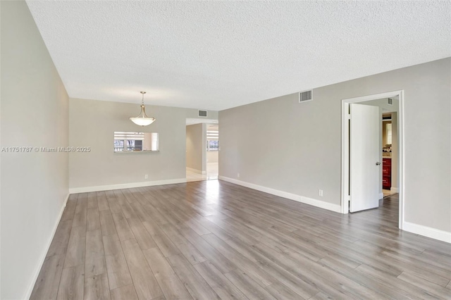 empty room with light wood-type flooring, visible vents, and a textured ceiling