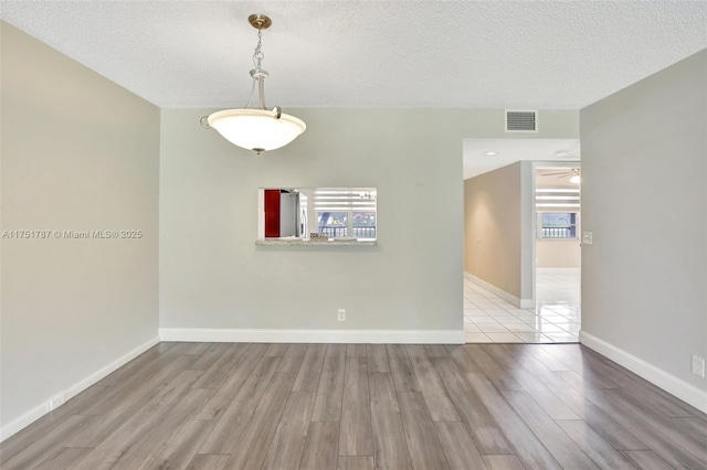 unfurnished room with light wood-type flooring, visible vents, a textured ceiling, and baseboards