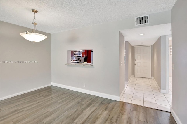 interior space with light wood-type flooring, visible vents, a textured ceiling, and baseboards