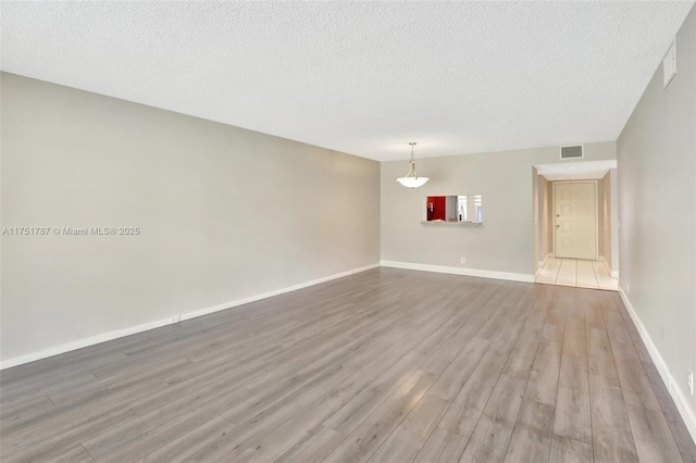 spare room with visible vents, a textured ceiling, baseboards, and wood finished floors