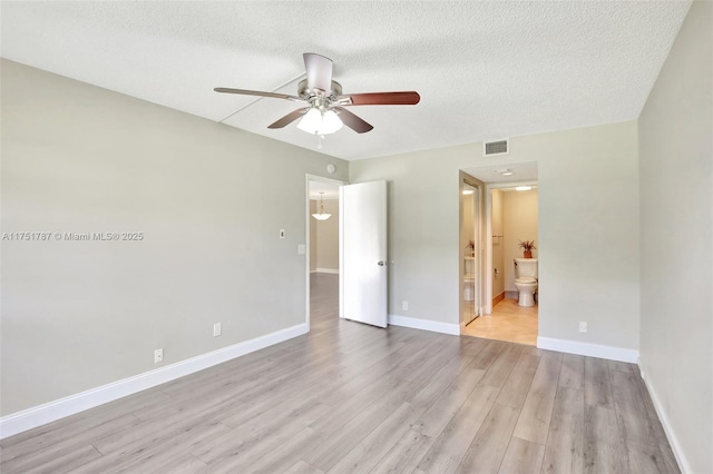 unfurnished bedroom with a textured ceiling, connected bathroom, visible vents, baseboards, and light wood-style floors