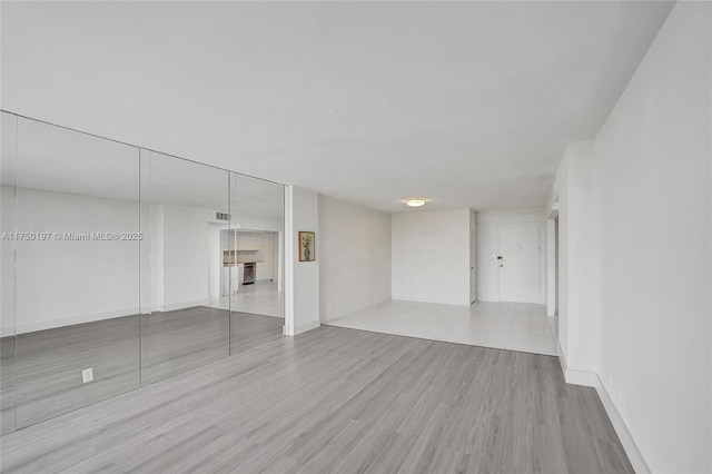 spare room featuring light wood finished floors, visible vents, and baseboards