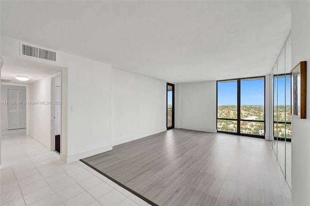 spare room with light wood-style floors, expansive windows, visible vents, and baseboards