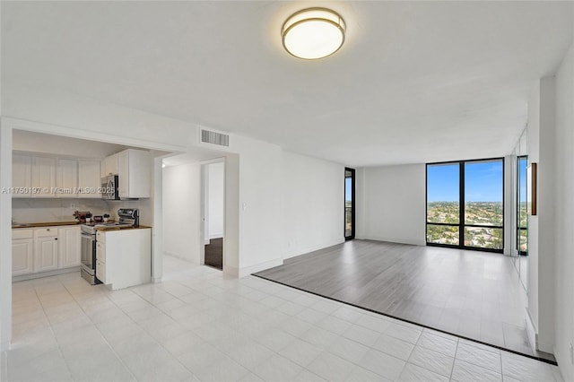 unfurnished living room featuring light tile patterned floors, baseboards, visible vents, and a wall of windows