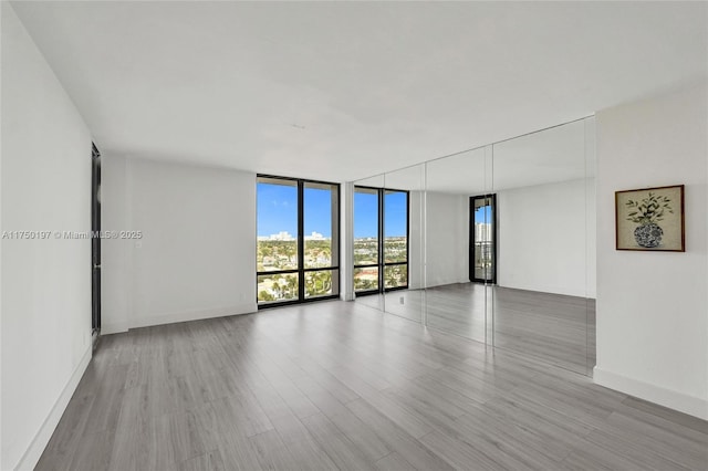 empty room with expansive windows, baseboards, and light wood-style floors