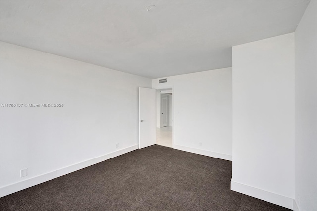 spare room featuring visible vents, dark carpet, and baseboards