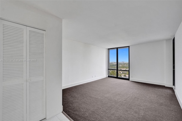 unfurnished bedroom with expansive windows, baseboards, dark colored carpet, and a closet