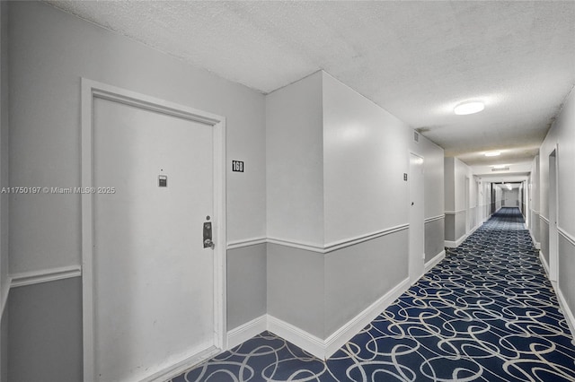 hallway with carpet flooring, a textured ceiling, and baseboards