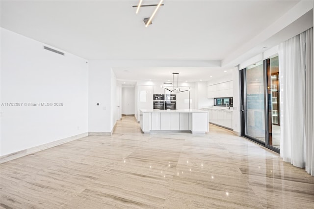 unfurnished living room featuring a notable chandelier, a sink, visible vents, and baseboards