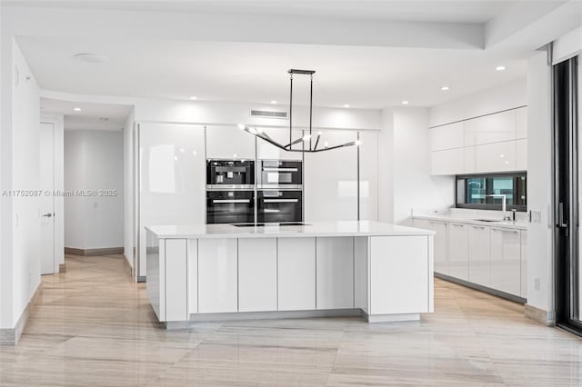 kitchen featuring modern cabinets, light countertops, stainless steel double oven, and decorative light fixtures