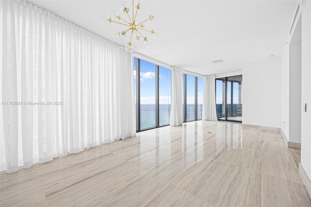 spare room featuring a chandelier, a wall of windows, a water view, and a wealth of natural light