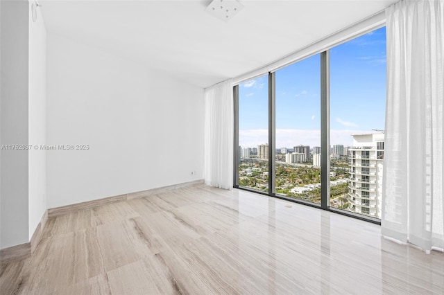 spare room with floor to ceiling windows, a city view, and baseboards