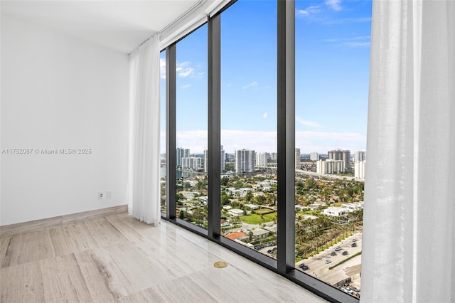 unfurnished room with a wall of windows, a view of city, a healthy amount of sunlight, and baseboards