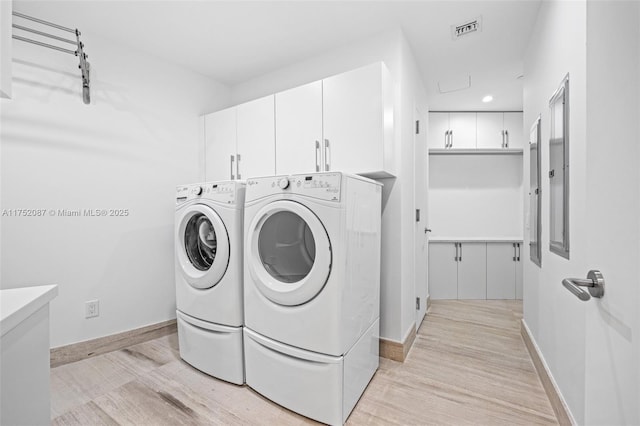 washroom featuring light wood-type flooring, cabinet space, washing machine and dryer, and visible vents