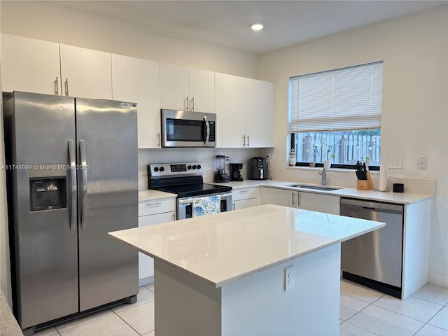 kitchen with light stone counters, a sink, white cabinets, appliances with stainless steel finishes, and a center island