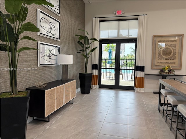 doorway to outside featuring light tile patterned floors, brick wall, french doors, and a high ceiling