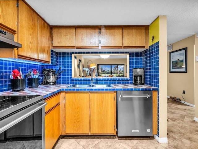 kitchen with under cabinet range hood, a sink, appliances with stainless steel finishes, tile counters, and decorative backsplash