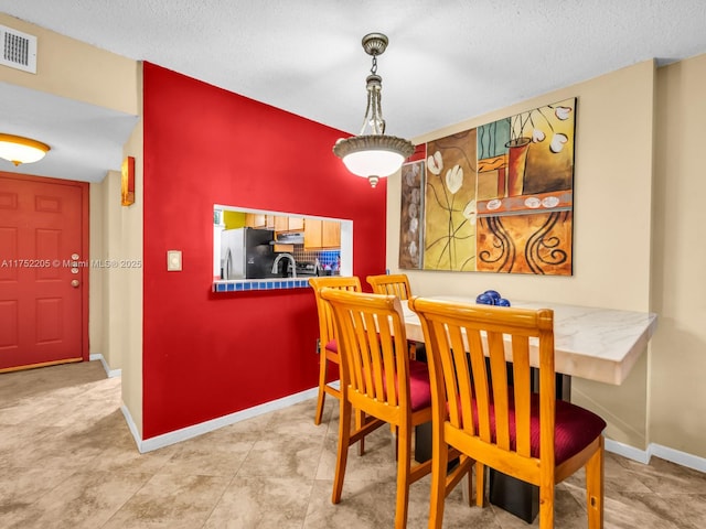 dining area with visible vents, a textured ceiling, and baseboards