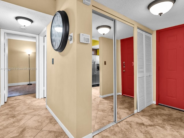 hallway featuring a textured ceiling, baseboards, and light tile patterned floors