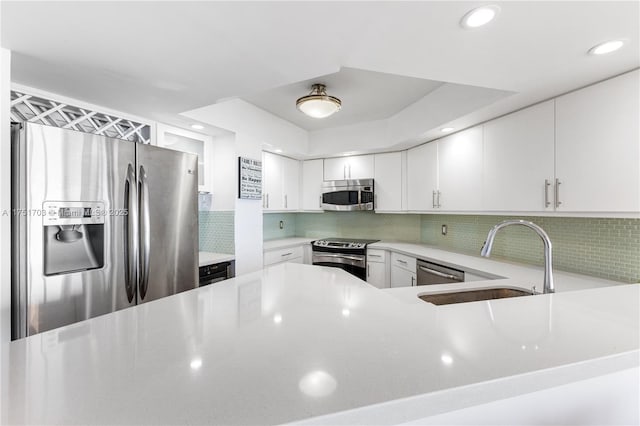 kitchen with light countertops, backsplash, appliances with stainless steel finishes, white cabinets, and a sink