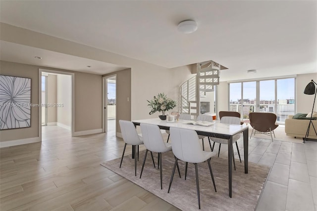 dining area featuring a wall of windows, stairway, light wood-style flooring, and baseboards