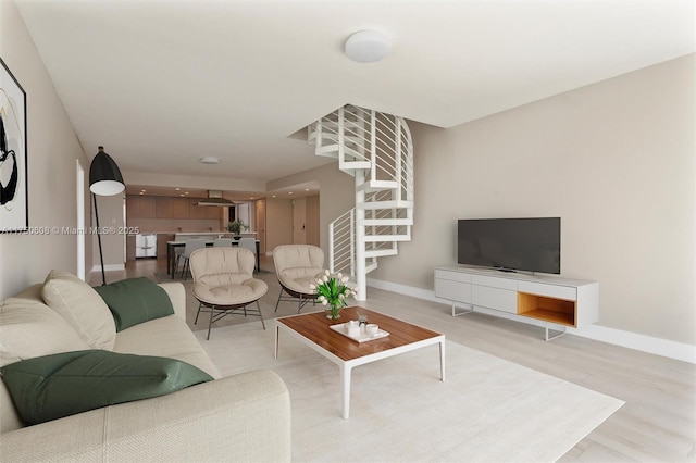 living area with light wood-style floors, stairway, and baseboards