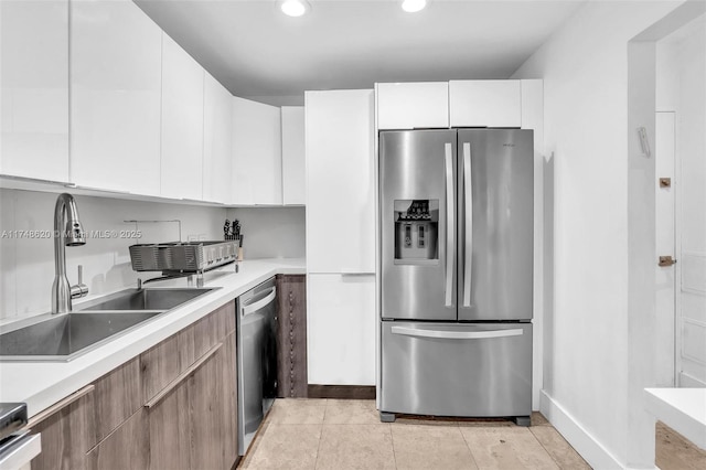 kitchen with appliances with stainless steel finishes, light countertops, a sink, and white cabinetry