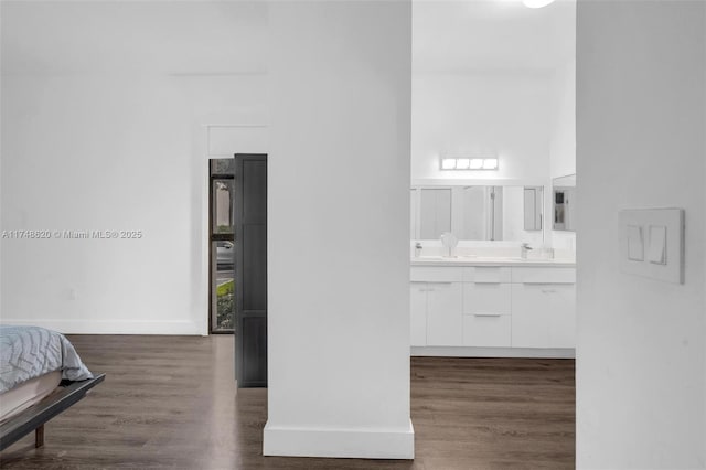 full bath featuring double vanity, a sink, baseboards, and wood finished floors