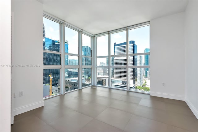 spare room featuring expansive windows, a view of city, and baseboards