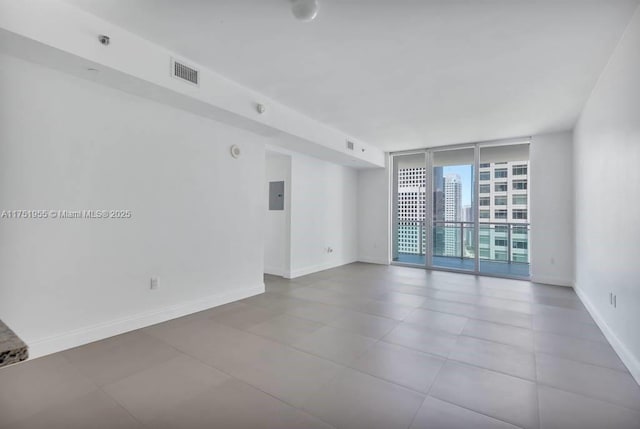 unfurnished room with a city view, visible vents, baseboards, electric panel, and a wall of windows