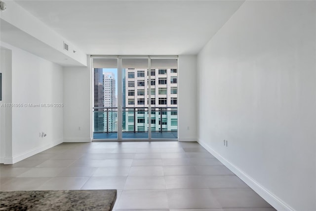 tiled spare room with expansive windows, visible vents, baseboards, and a view of city