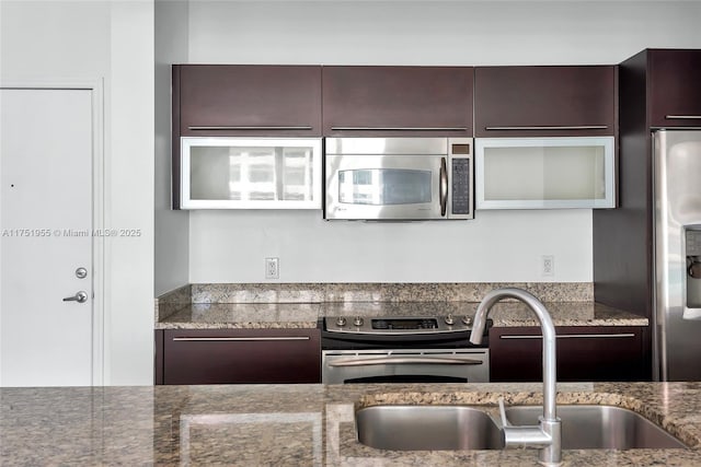 kitchen with appliances with stainless steel finishes, stone counters, dark brown cabinetry, and a sink