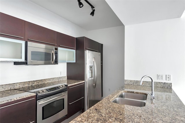 kitchen with stainless steel appliances, stone countertops, a sink, and rail lighting