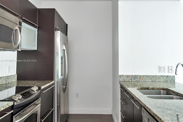 kitchen with appliances with stainless steel finishes, baseboards, a sink, and light stone counters