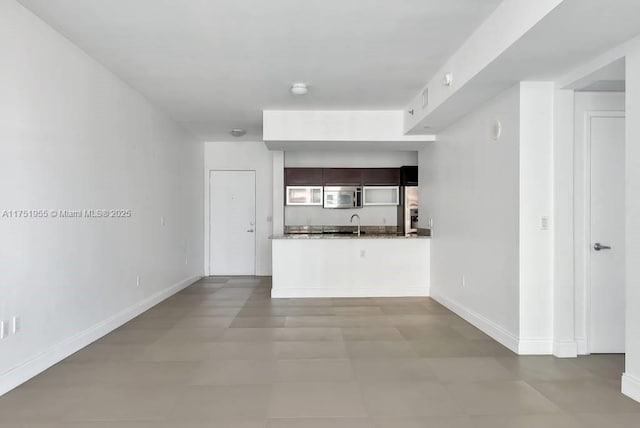 kitchen with baseboards, dark countertops, open floor plan, a peninsula, and stainless steel appliances