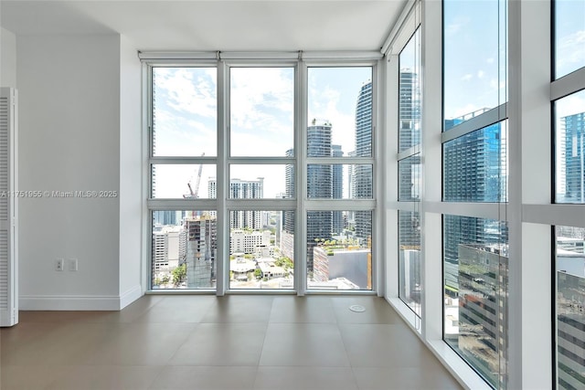 interior space featuring tile patterned flooring, floor to ceiling windows, a city view, and baseboards