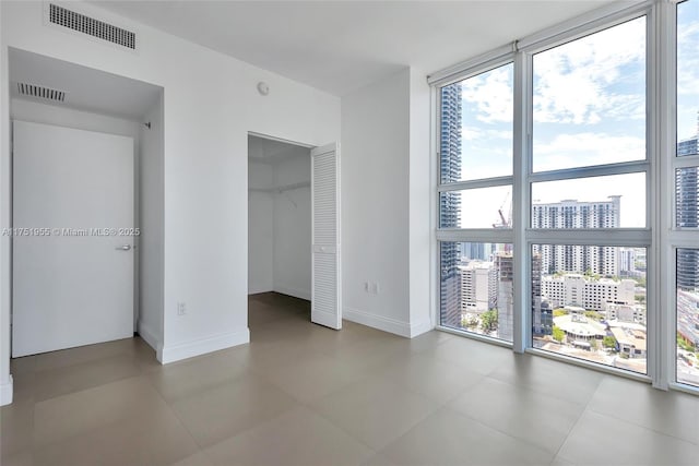 unfurnished bedroom with baseboards, floor to ceiling windows, visible vents, and a city view