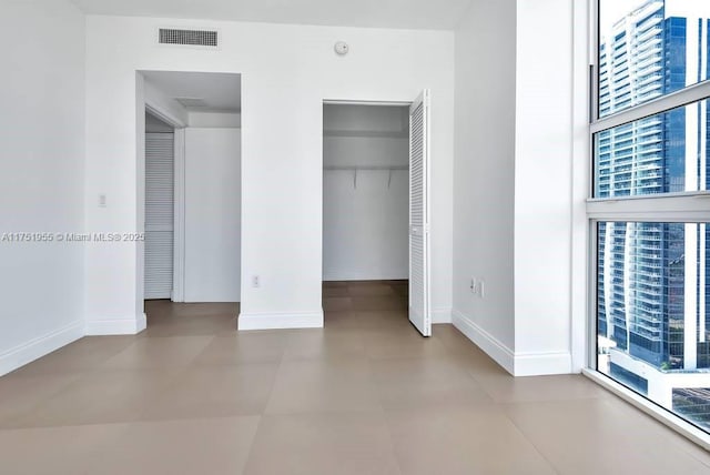 unfurnished bedroom featuring baseboards, a view of city, visible vents, and a closet