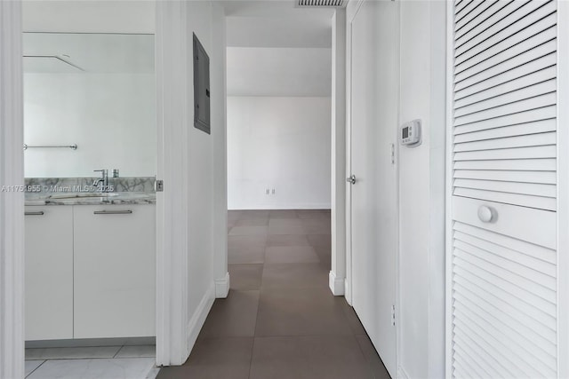 corridor featuring baseboards, electric panel, visible vents, and a sink