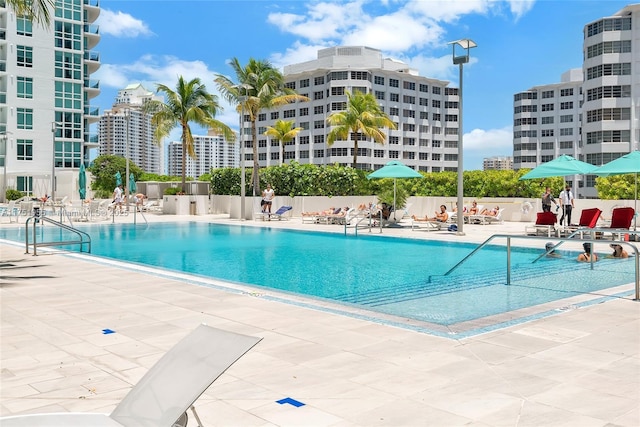 pool with a patio, fence, and a city view